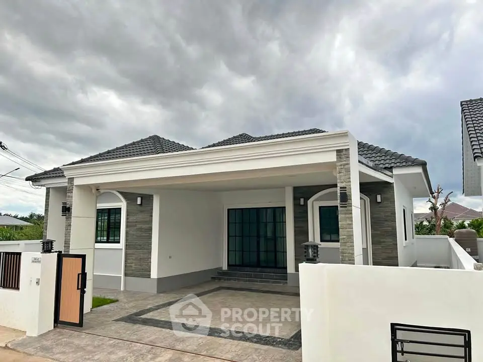 Modern single-story house with elegant facade and spacious driveway under cloudy sky.