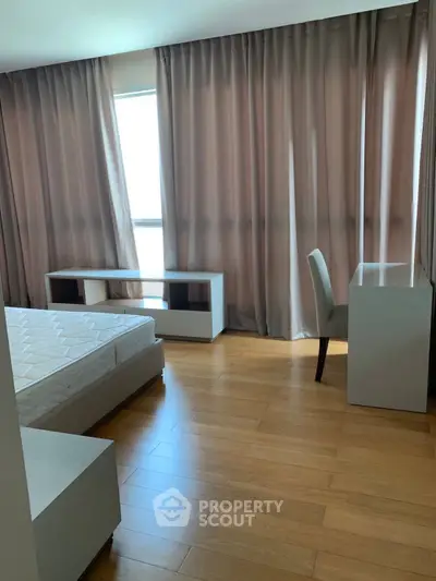 Spacious bedroom with wooden flooring and modern furniture, featuring large windows with elegant curtains.