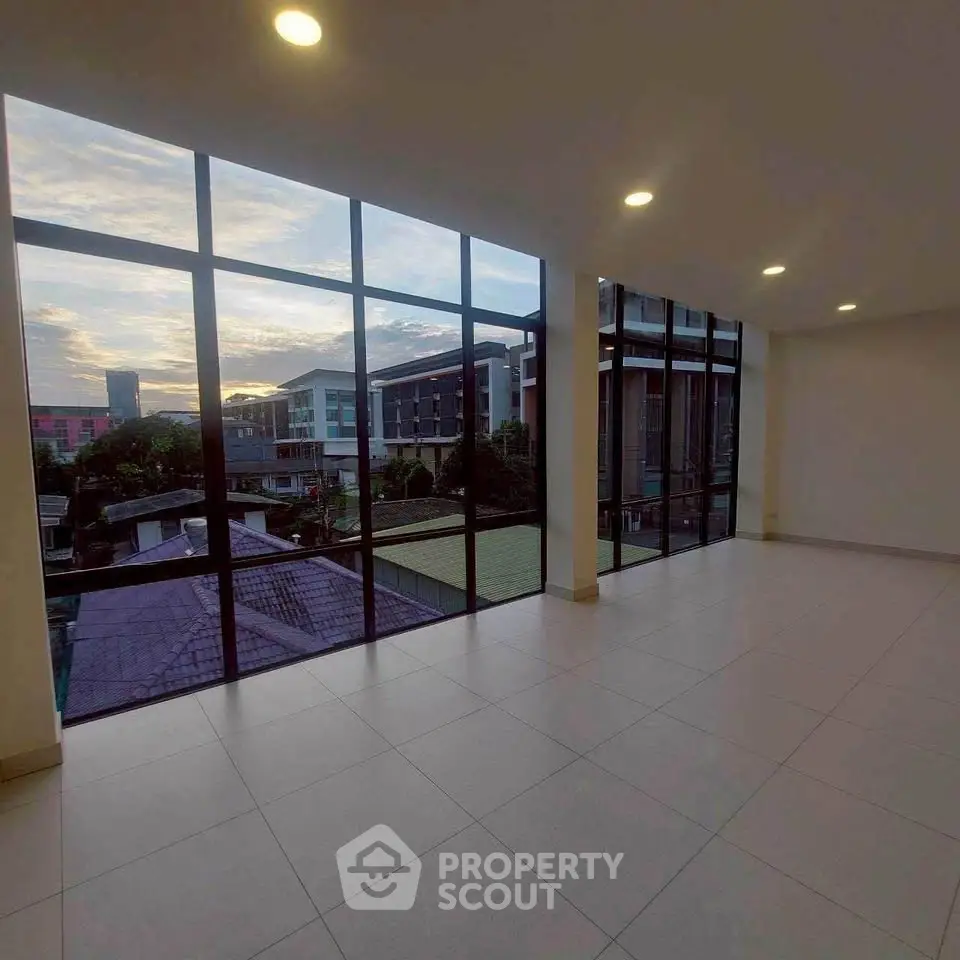 Spacious room with floor-to-ceiling windows offering stunning city views at sunset.