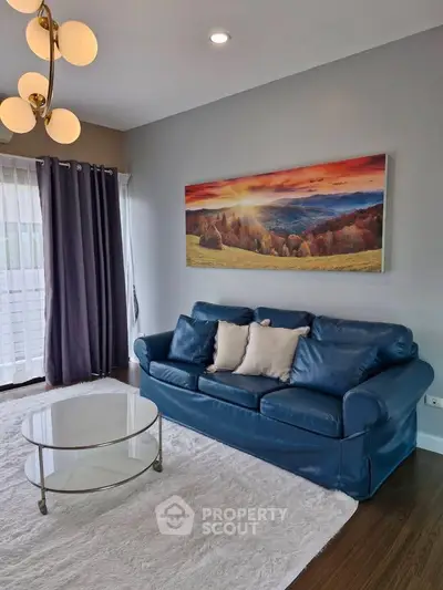 Stylish living room with blue sofa, modern lighting, and scenic wall art.