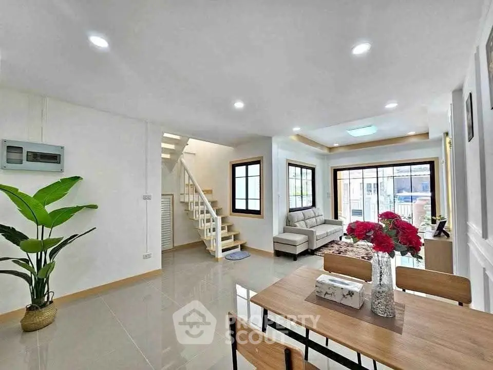 Modern open-plan living and dining area with staircase and large windows.