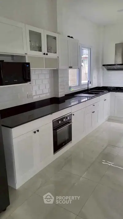 Modern kitchen with sleek white cabinets and black countertops, featuring built-in oven and microwave.