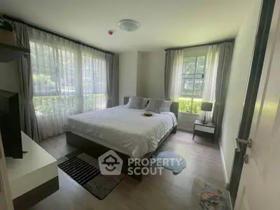 Cozy bedroom with large windows and modern decor in a serene setting.