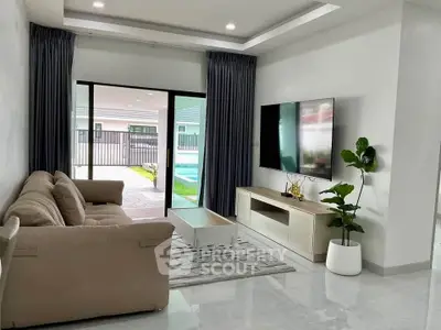 Modern living room with large TV, cozy sofa, and pool view through sliding glass doors.