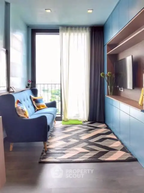 Modern living room with stylish blue sofa and geometric rug, featuring a wall-mounted TV and balcony view.