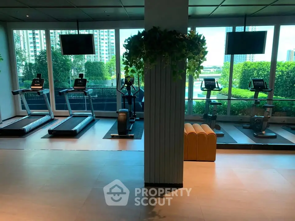 Modern gym with treadmills and exercise bikes overlooking lush greenery and cityscape.