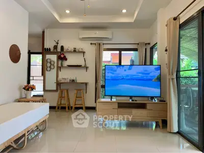 Modern living room with stylish decor, large TV, and natural light from windows and glass doors.