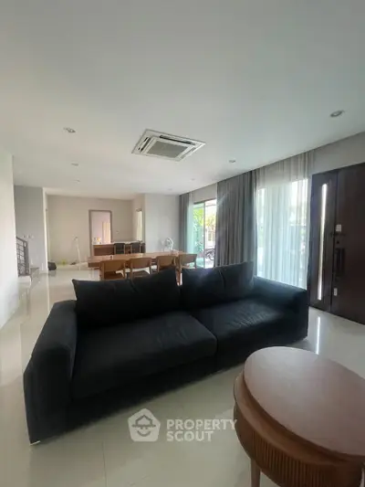 Spacious modern living room with large sofa and dining area, featuring natural light and elegant decor.