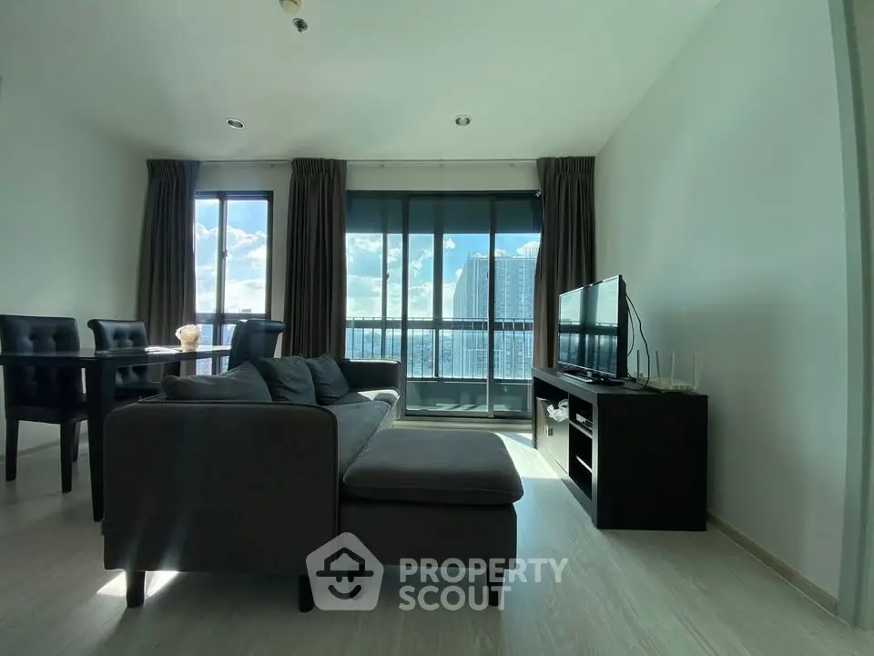 Modern living room with large windows offering stunning city views, featuring a stylish sofa and entertainment unit.