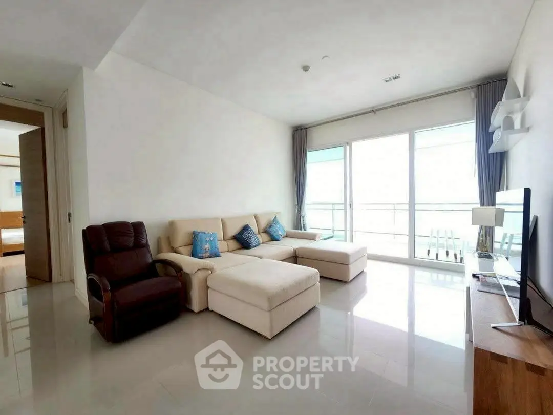 Spacious living room with modern furniture and large windows offering natural light and balcony access.