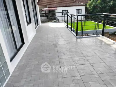 Spacious balcony with modern railing and tiled flooring, overlooking a lush green garden.