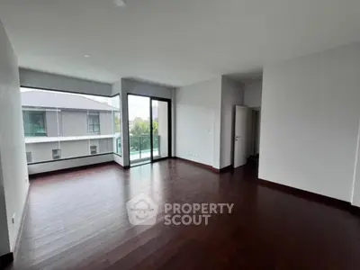 Spacious modern living room with dark wood flooring and large windows offering natural light.