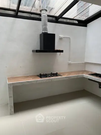 Modern kitchen with sleek gas stove and marble countertops under a skylight.
