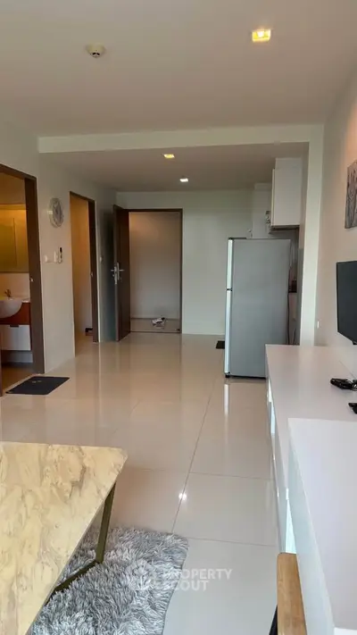 Modern apartment interior with sleek kitchen and open living area, featuring a marble table and stainless steel fridge.