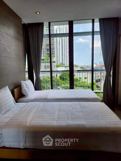 Modern bedroom with twin beds and city view through large windows.