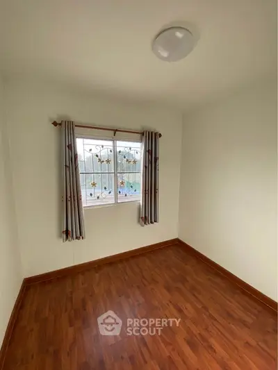 Spacious empty room with wooden flooring and window view, perfect for customization.