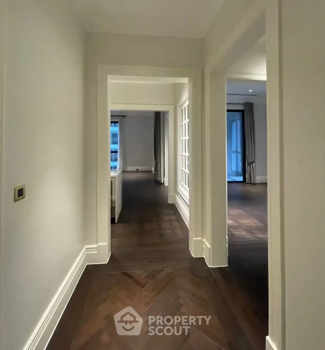 Elegant hallway with dark wood flooring and white walls leading to spacious rooms