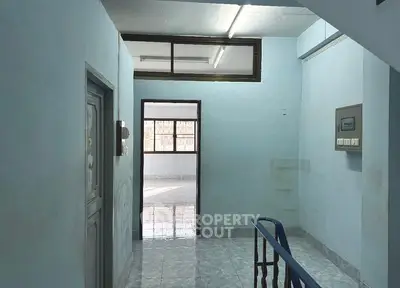Spacious hallway with blue walls and tiled flooring, leading to a sunlit room.