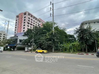 Urban street view with modern apartment building and lush greenery, ideal for city living.