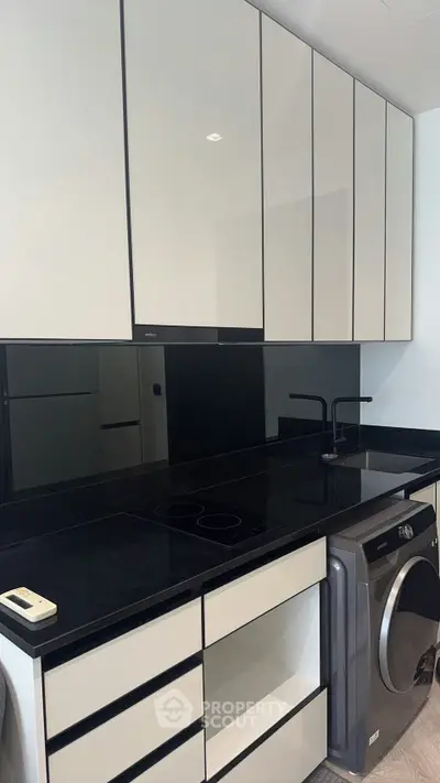 Modern kitchen with sleek black countertops and built-in appliances, featuring a washing machine and minimalist design.
