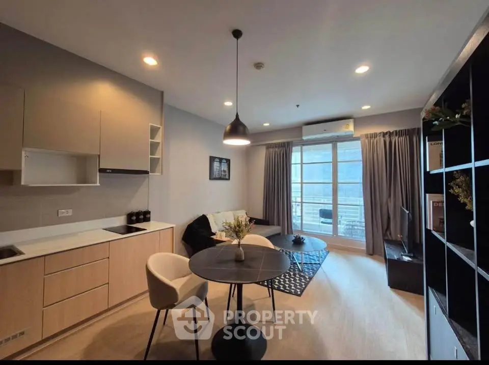 Modern living room with open kitchen and balcony view, featuring stylish furniture and natural light.