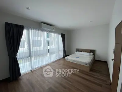 Spacious bedroom with large windows and wooden flooring in modern apartment.