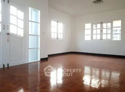 Spacious empty room with polished wooden floors and large windows.