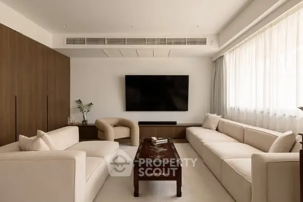 Elegant living room with modern furniture and large TV, featuring natural light and stylish decor.