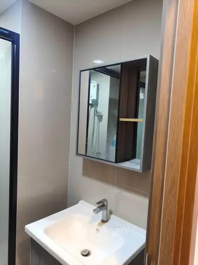 Modern bathroom with sleek sink and mirrored cabinet, featuring a shower area with glass door.