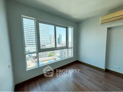 Spacious room with large window offering stunning city views and modern wooden flooring.