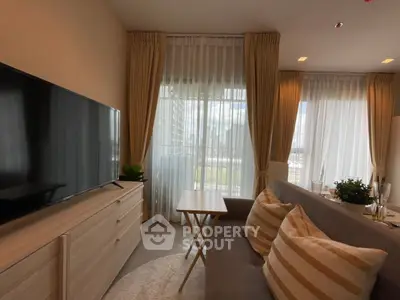 Elegant living room with ample natural light, featuring a large TV, cozy sofa, and stylish curtains leading to a sunlit balcony.