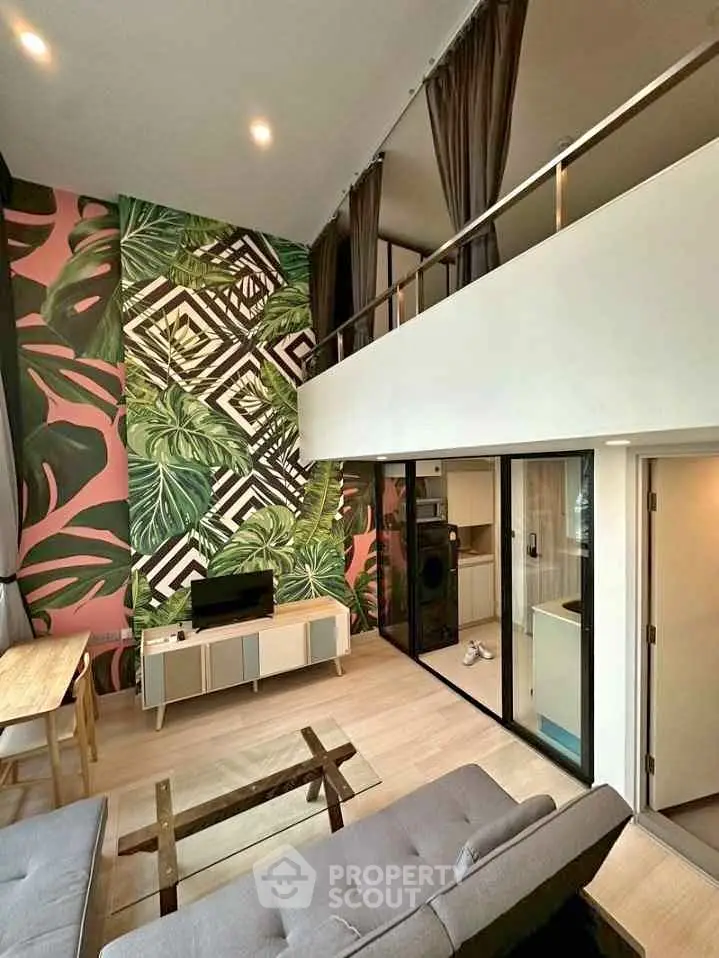 Stylish modern living room with high ceiling and tropical accent wall, featuring a cozy loft area.