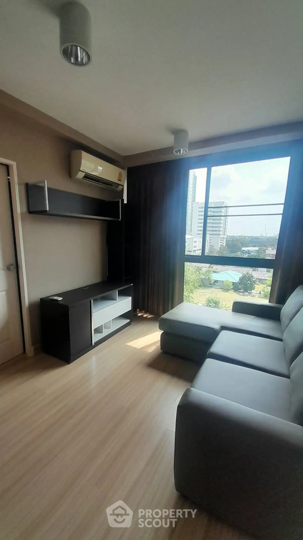 Modern living room with large window and city view, featuring sleek furniture and natural light.