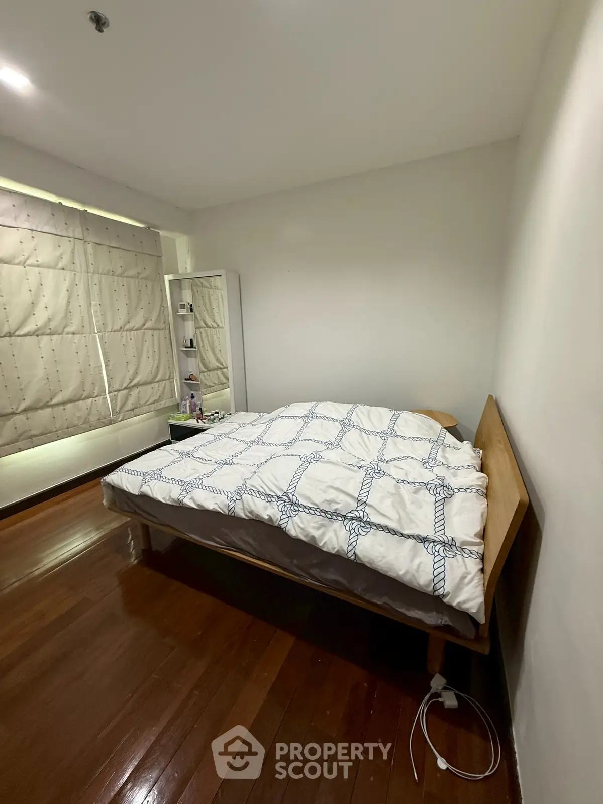 Cozy bedroom with wooden flooring and modern decor in a well-lit apartment.