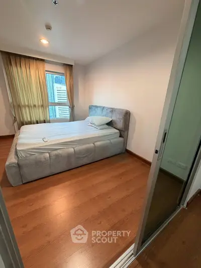 Cozy bedroom with wooden flooring and large window in modern apartment