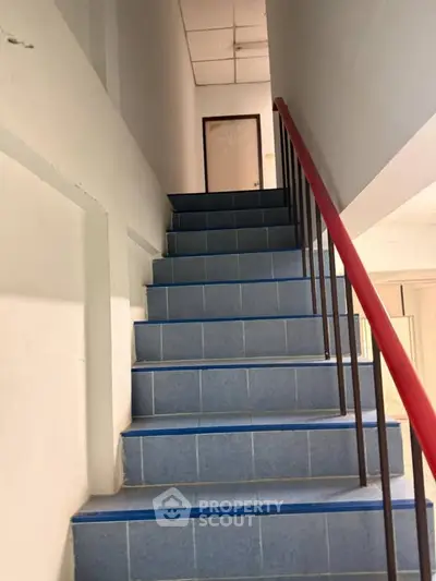 Staircase with blue tiles and red handrail in a residential building