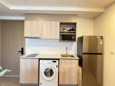 Modern kitchen with washing machine, microwave, and fridge in compact layout.
