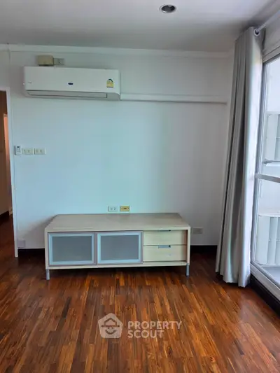 Modern living room with wooden flooring and air conditioning unit, featuring a sleek storage cabinet.