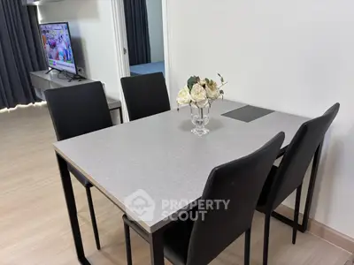 Modern dining area with sleek table and chairs, adjacent to a cozy living room with TV.