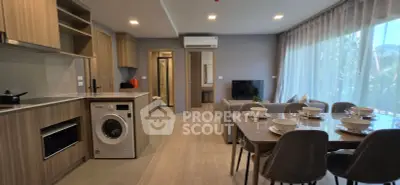 Modern open-plan living room with kitchen and dining area, featuring sleek appliances and large windows.
