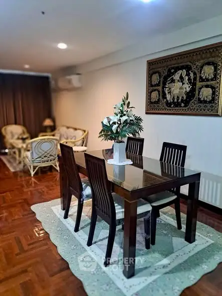 Elegant dining area with wooden table and chairs, featuring a decorative wall art and cozy seating in the background.
