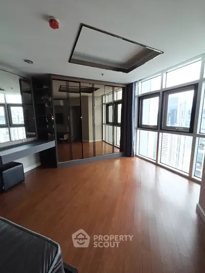 Spacious modern living room with hardwood floors and large windows offering city views.