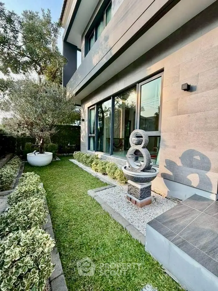 Modern home exterior with lush garden and stylish sculpture, perfect for serene living.