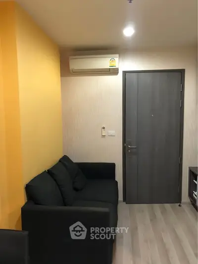 Modern living room with sleek black sofa and vibrant yellow accent wall, featuring air conditioning and stylish flooring.