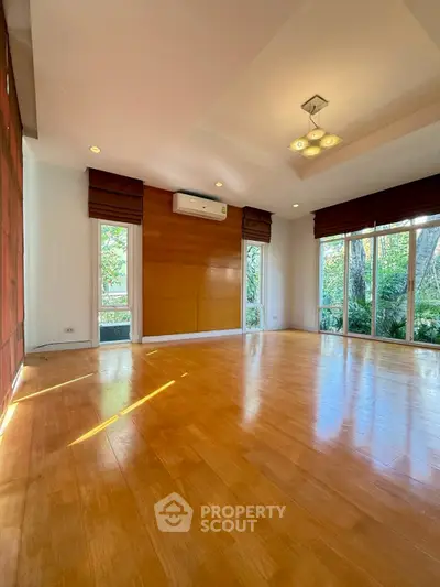 Spacious living room with wooden flooring and large windows offering garden views.