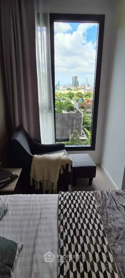 Chic bedroom with stunning city view through large window, featuring cozy chair and modern decor.