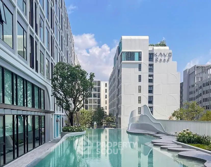 Modern apartment complex with sleek pool and contemporary architecture under a clear blue sky.