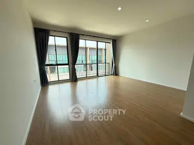 Spacious empty living room with large windows and wooden flooring, perfect for customization.