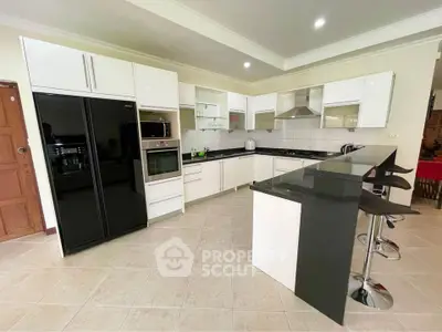 Modern kitchen with sleek black countertops and white cabinetry, featuring built-in appliances and breakfast bar.