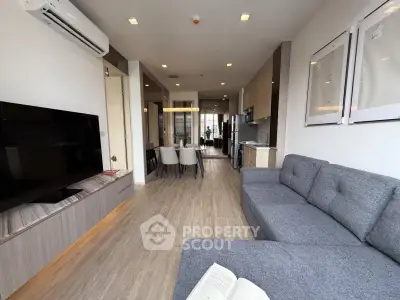 Modern living room with open layout, featuring a sleek sofa, wall-mounted TV, and dining area in a stylish apartment.